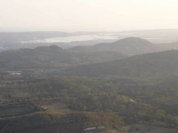 "Der Blick vom Hügelkamm herab auf die Bucht von Santiago, für die sich kein Mensch hier interessierte, war in der Tat großartig, man schaute über Stadt Land Fluß bis weit ins karibische Meer hinein. Wie hell es glitzerte vom Horizont!
Und wie dunkel die Landschaft davor sich breitete, jedenfalls dort, wo der Schatten einer Wolke darüberlag!" - Blick von Puerto Boniato auf die Bucht von Santiago